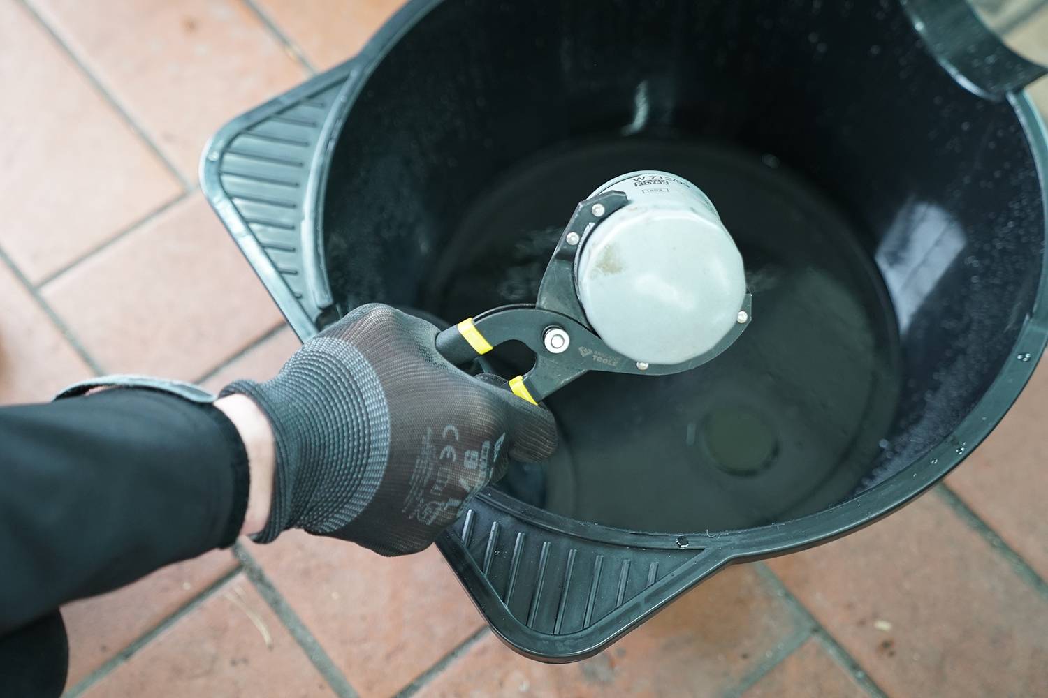 'A person wearing a glove is holding a metallic kitchen utensil over a black container.'