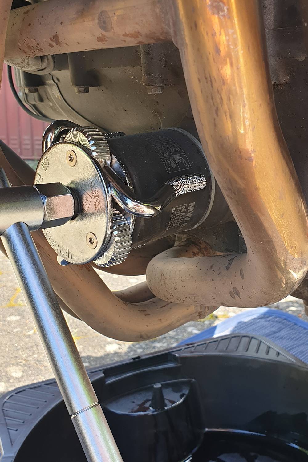 Engine oil filter change: Tool grips filter between exhaust pipes, collection tray underneath.