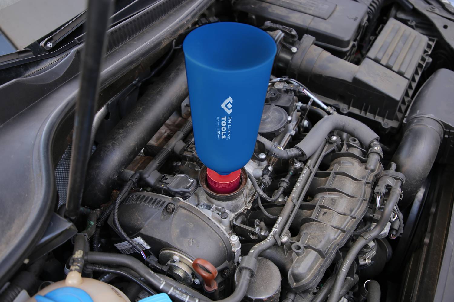 A blue funnel is inserted in the engine compartment of a car and is used for pouring in liquid, surrounded by automotive components.