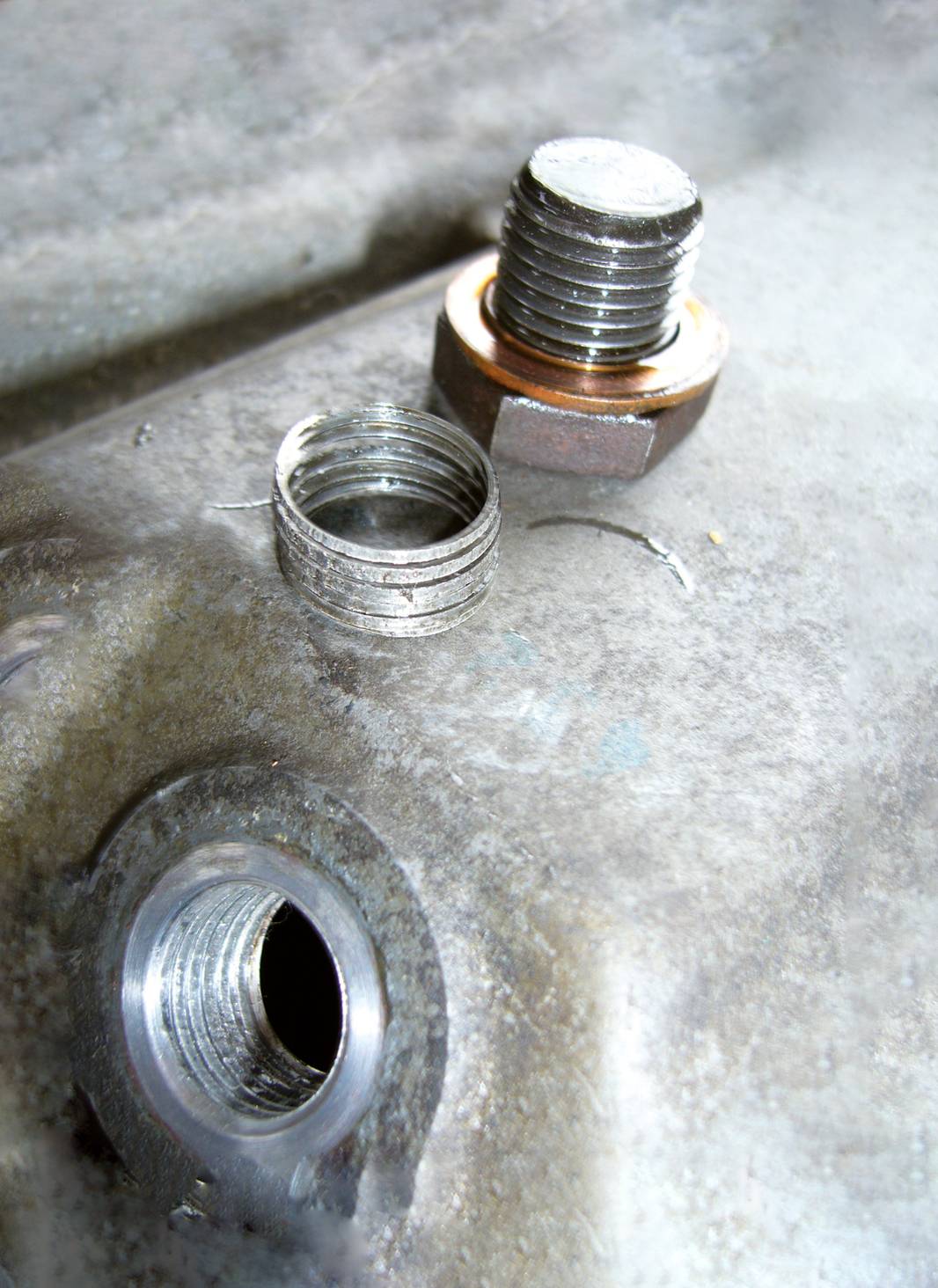 A sheared bolt with damaged threading beside an opening on a metal surface, indicating an assembly problem.