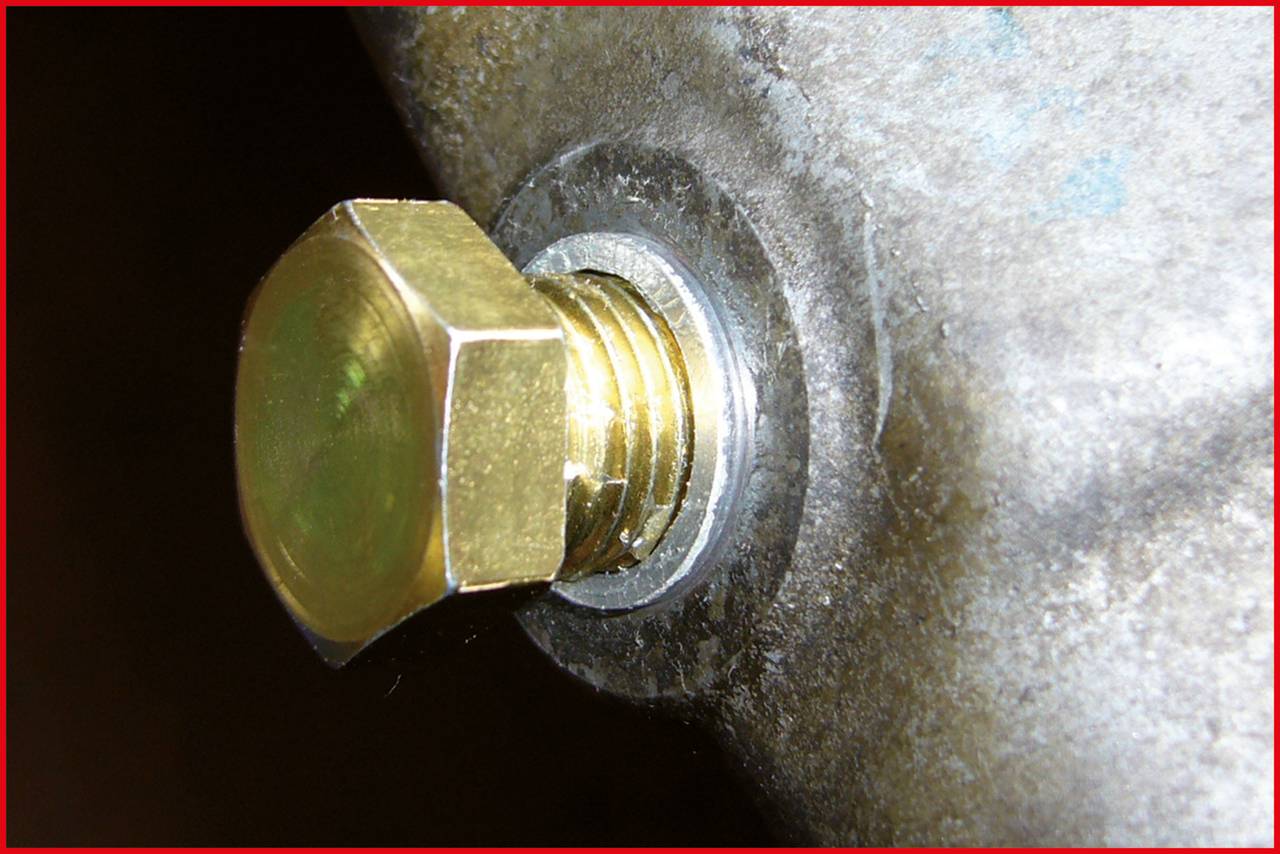 Close-up of a golden hexagonal bolt screwed into a grey metal housing.