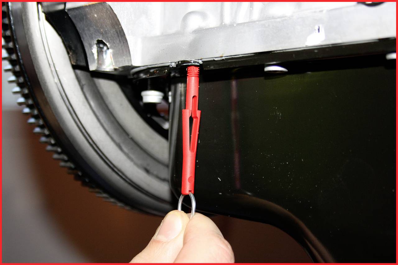 A hand pulls the red oil dipstick out of a vehicle engine to check the oil level.