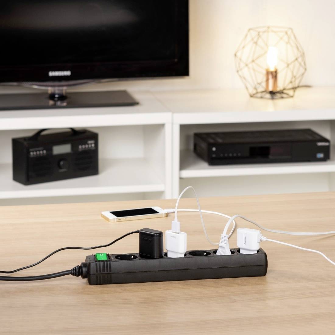 Multi-socket extension lead on a table with several connected chargers and cables, with a television and other devices in the background.