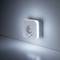 A night light in the shape of a socket with an integrated motion sensor illuminates on a wall and provides soft lighting.