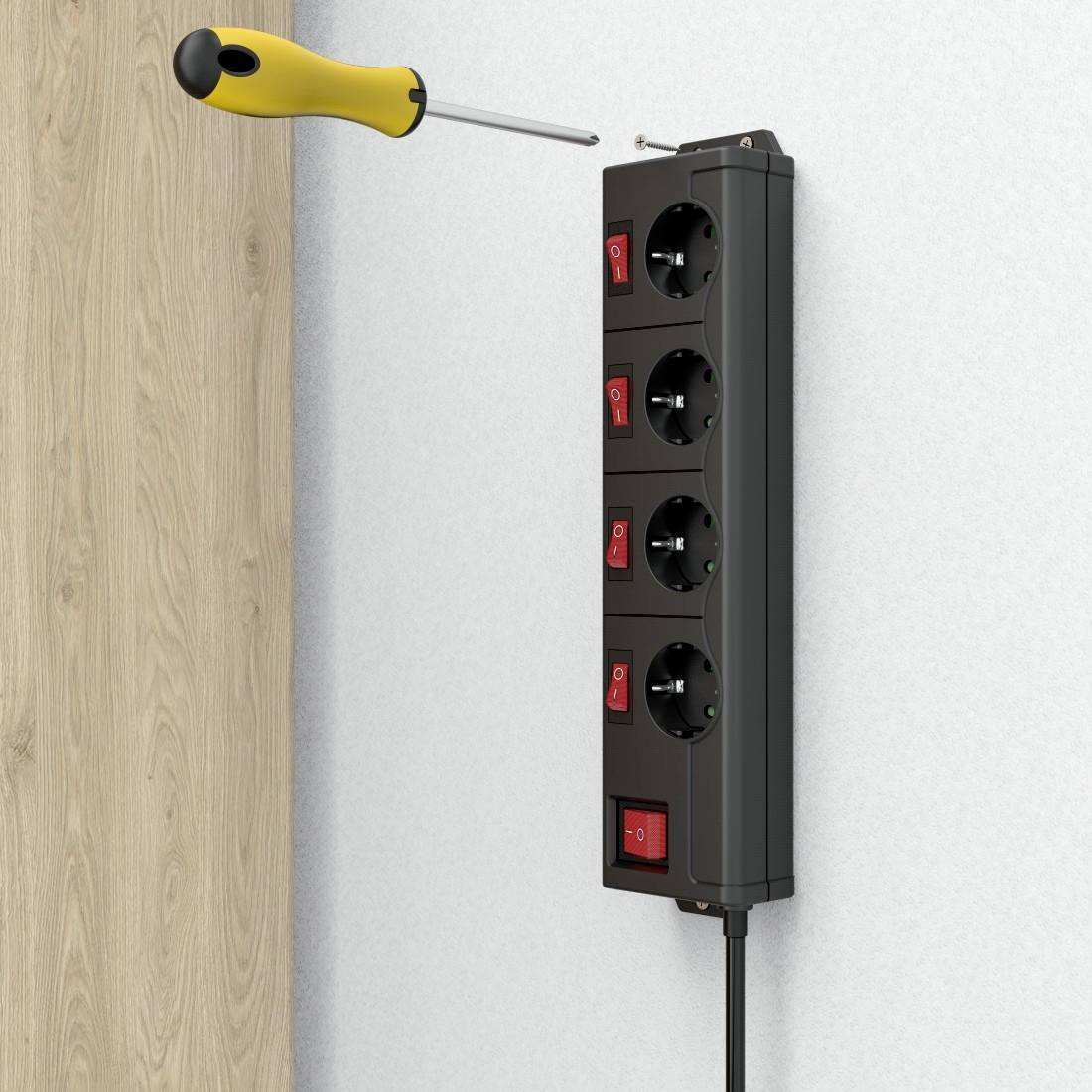 A black four-socket extension block is mounted on a wall. A screwdriver is being used to secure it.