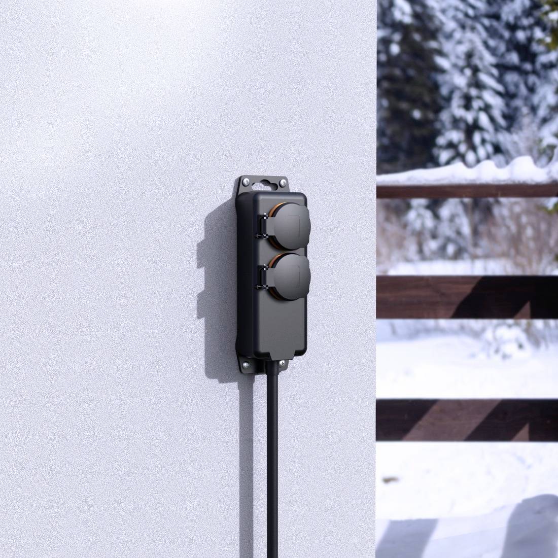 External socket with two connections on a wall, surrounded by a snow-covered landscape and wooden fence in the background.