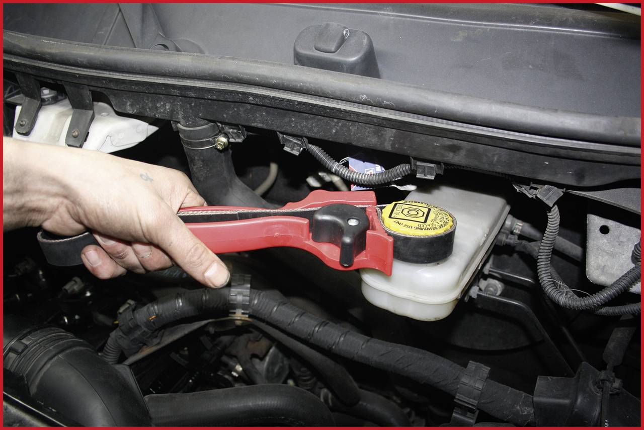 A hand is holding a pipe wrench and tightening the lid of a brake fluid reservoir in a vehicle's engine compartment.