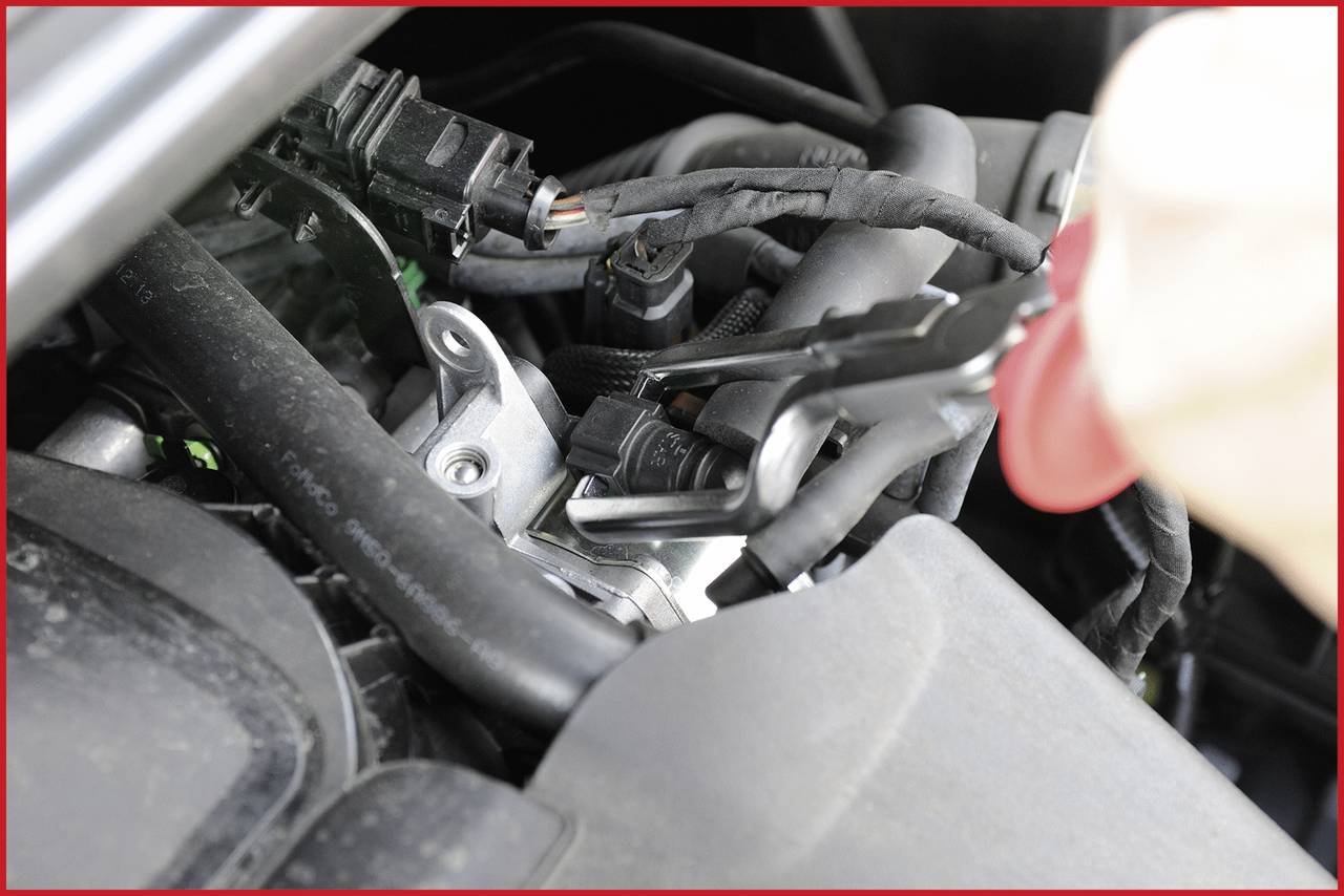Close-up of a car mechanic working on an engine with a tool, repairing or connecting cables.