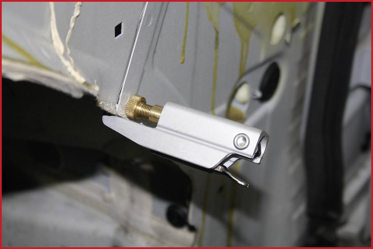 A metal component with a lever mechanism is attached to a vehicle frame. It appears to be an adjustment or tensioning mechanism.
