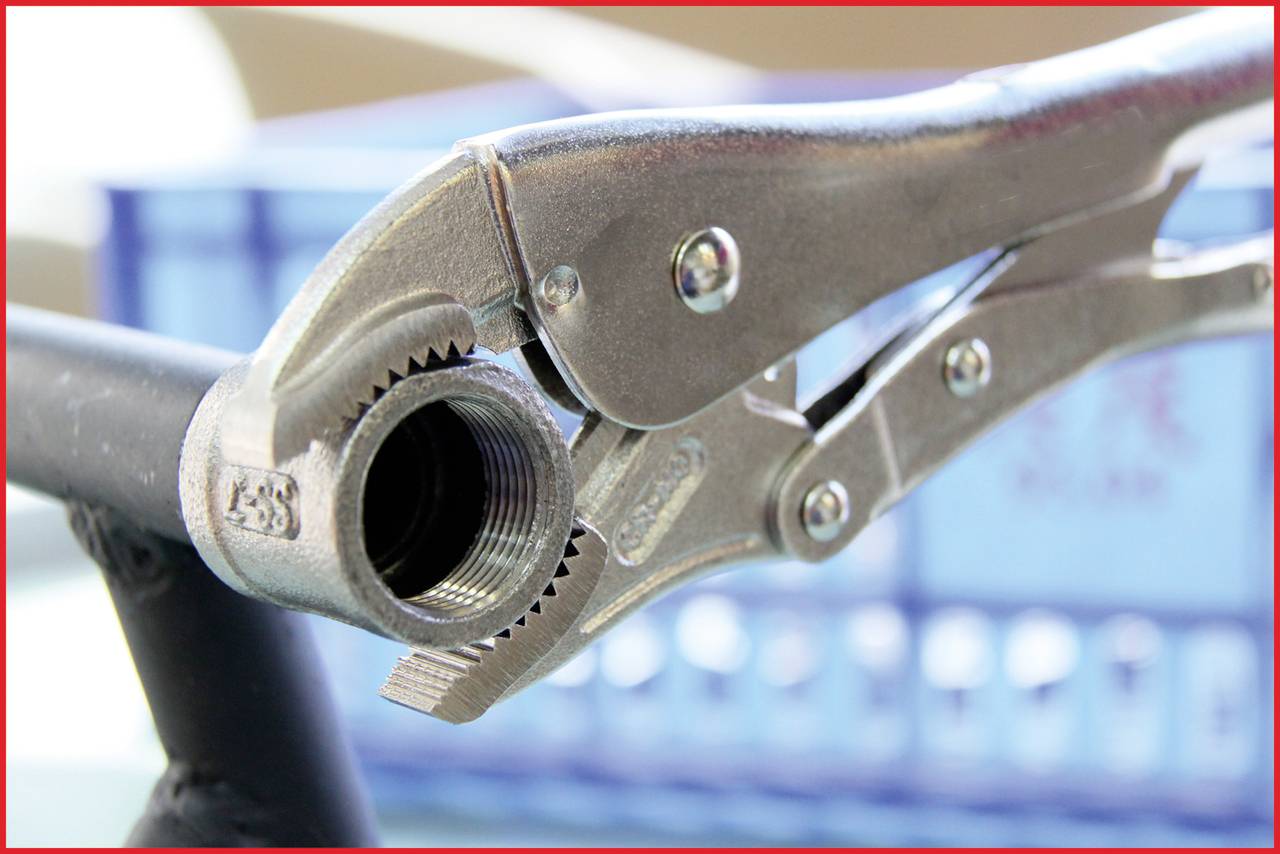 A silver pipe wrench grips a threaded metal pipe. In the background, a blurred blue box can be seen.