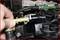 A hand is holding a yellow plastic hose and inserting it into a black mechanical component in an engine compartment.