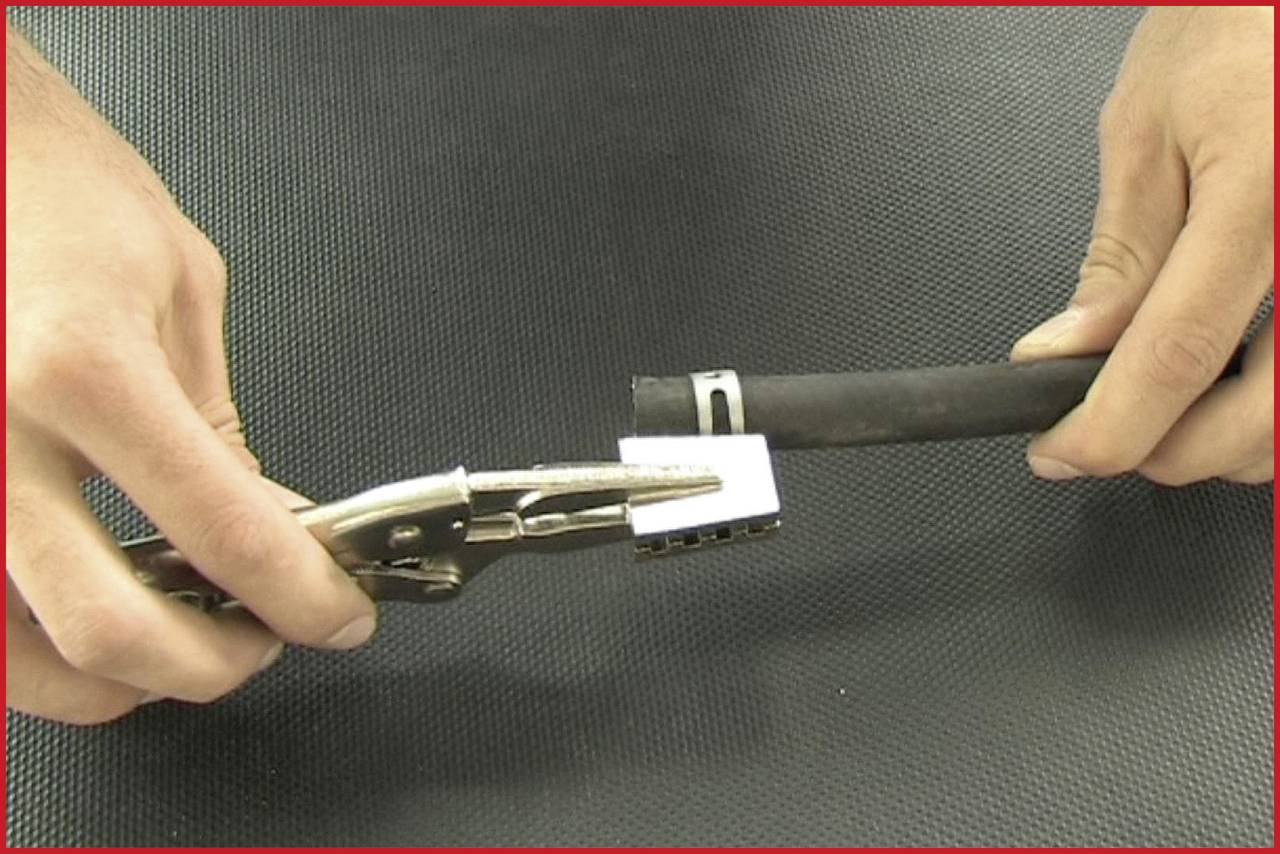 A person is holding a small rectangular object with pliers against a rubber tube. Hands and tools are visible.
