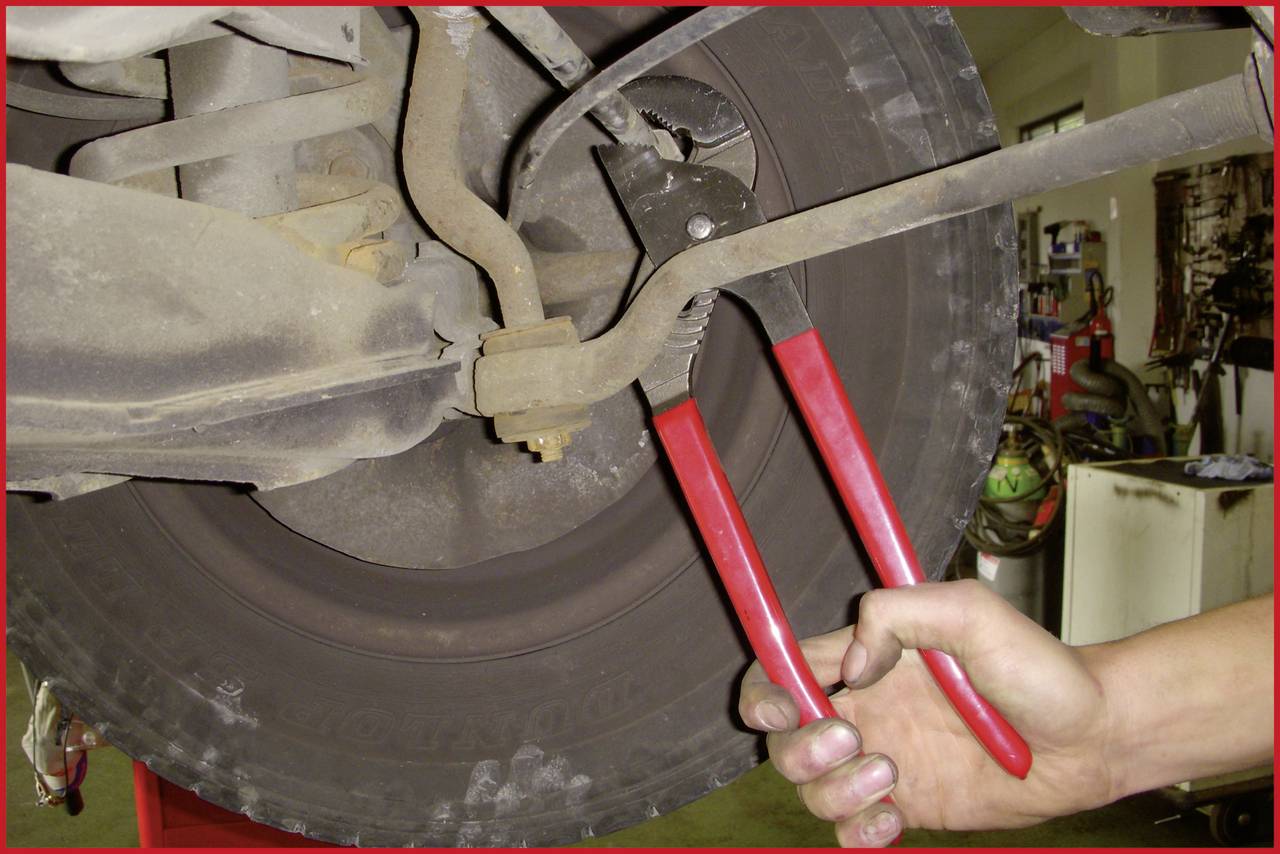A hand is using a red pair of pliers to repair or adjust something on a vehicle wheel. The focus is on working on the automotive part.