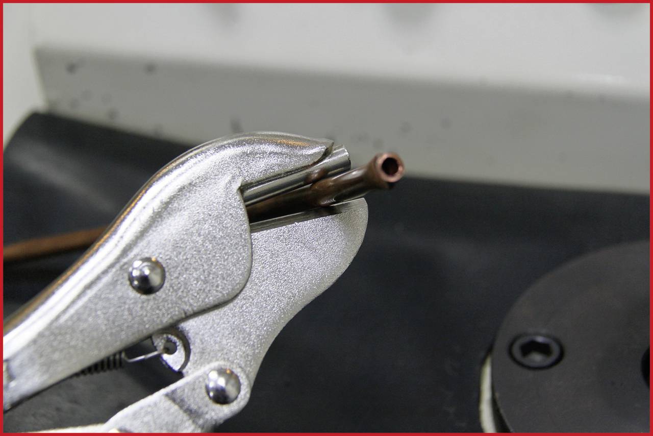 A pair of pliers is holding a thin metal pipe on a workbench. It is likely being used for repair or installation work.