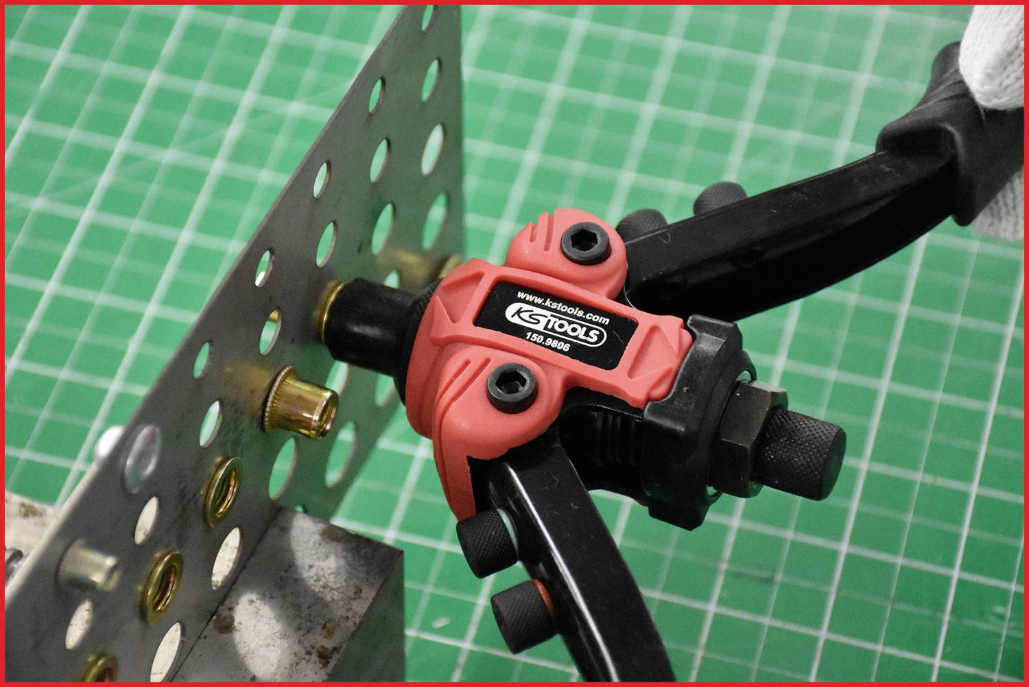 A pair of pliers inserts a brass rivet into a perforated metal sheet. The setting is a workbench with a green grid background.