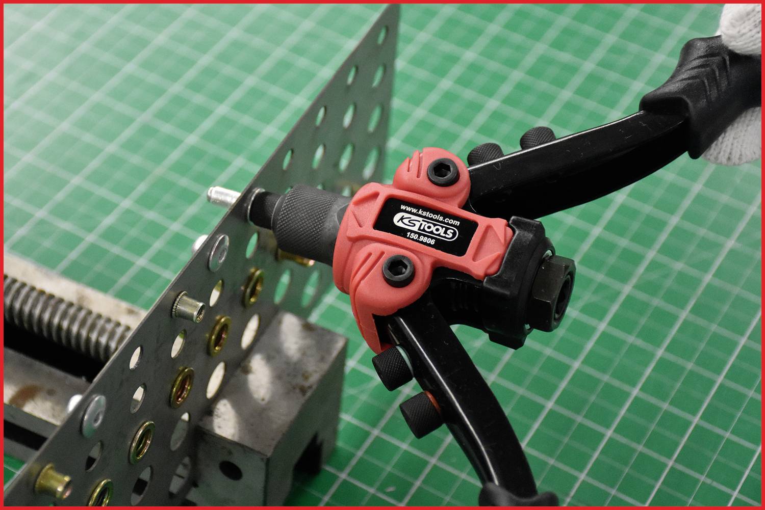 A red riveting plier is used to fasten a rivnut to a perforated sheet metal. Tool and workpiece on a green background.