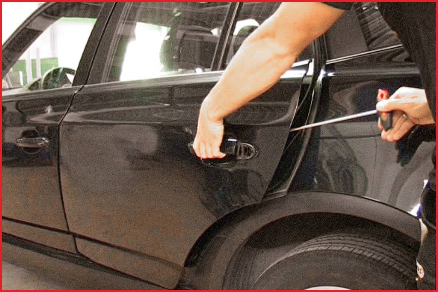A person is attempting to force open the door of a black car using a screwdriver.
