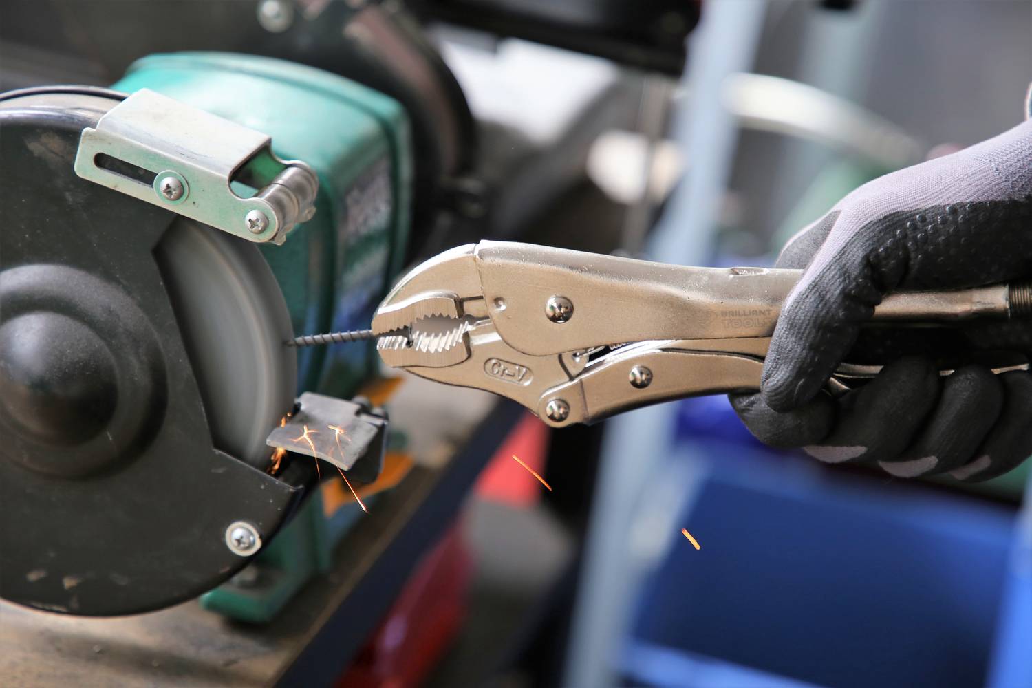 A person is grinding a drill with a bench grinder, sparks flying. The person is wearing gloves for safety.