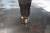 A drill bit is boring through a piece of metal on a workbench, with metal shavings visible.