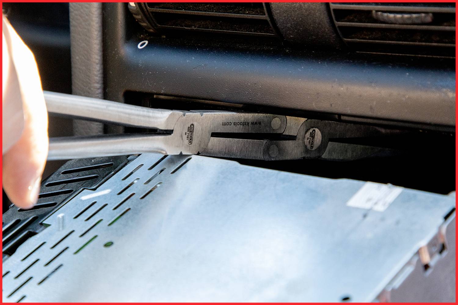 A hand is using a specialist tool to remove a car radio from a dashboard.