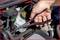 A hand is holding pliers and working on a car engine. A coolant reservoir is visible.
