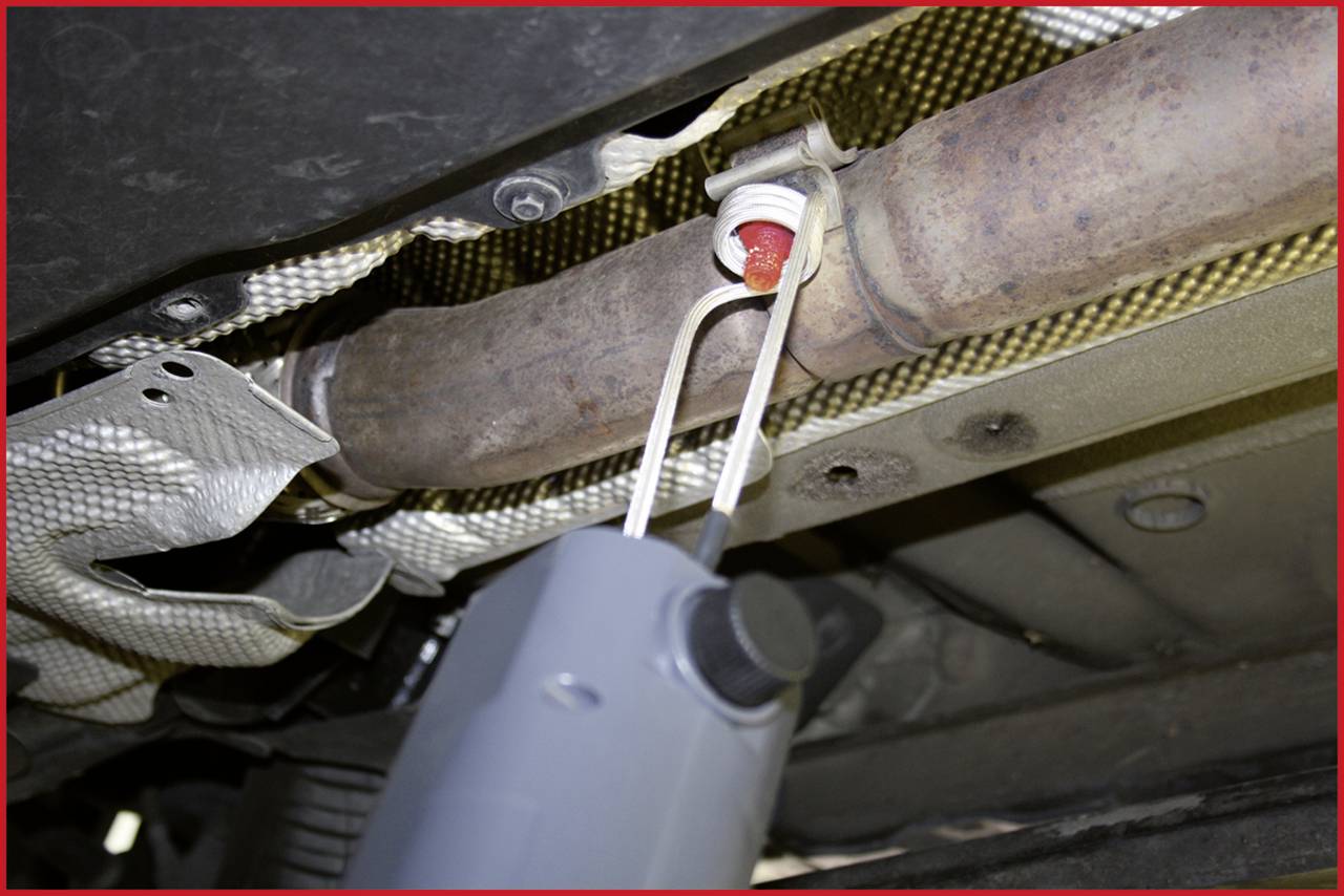 An exhaust pipe of a vehicle with a sensor that could measure temperature or pollutants is visible. The location appears to be underneath a car.