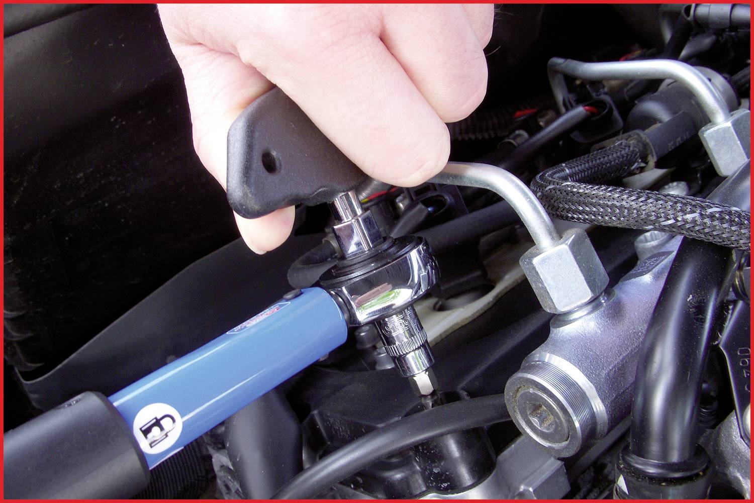 A person is tightening a bolt with a torque wrench in a vehicle's engine compartment.