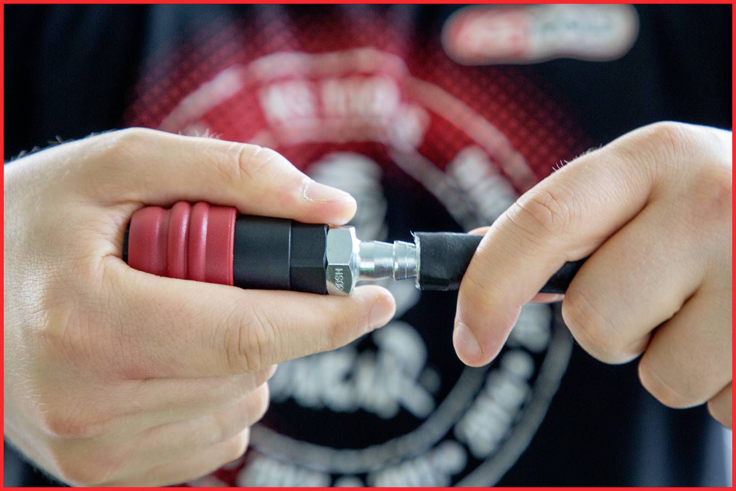 A person is holding the connection between a black hose and a metallic coupling in their hands, focusing on manual work.