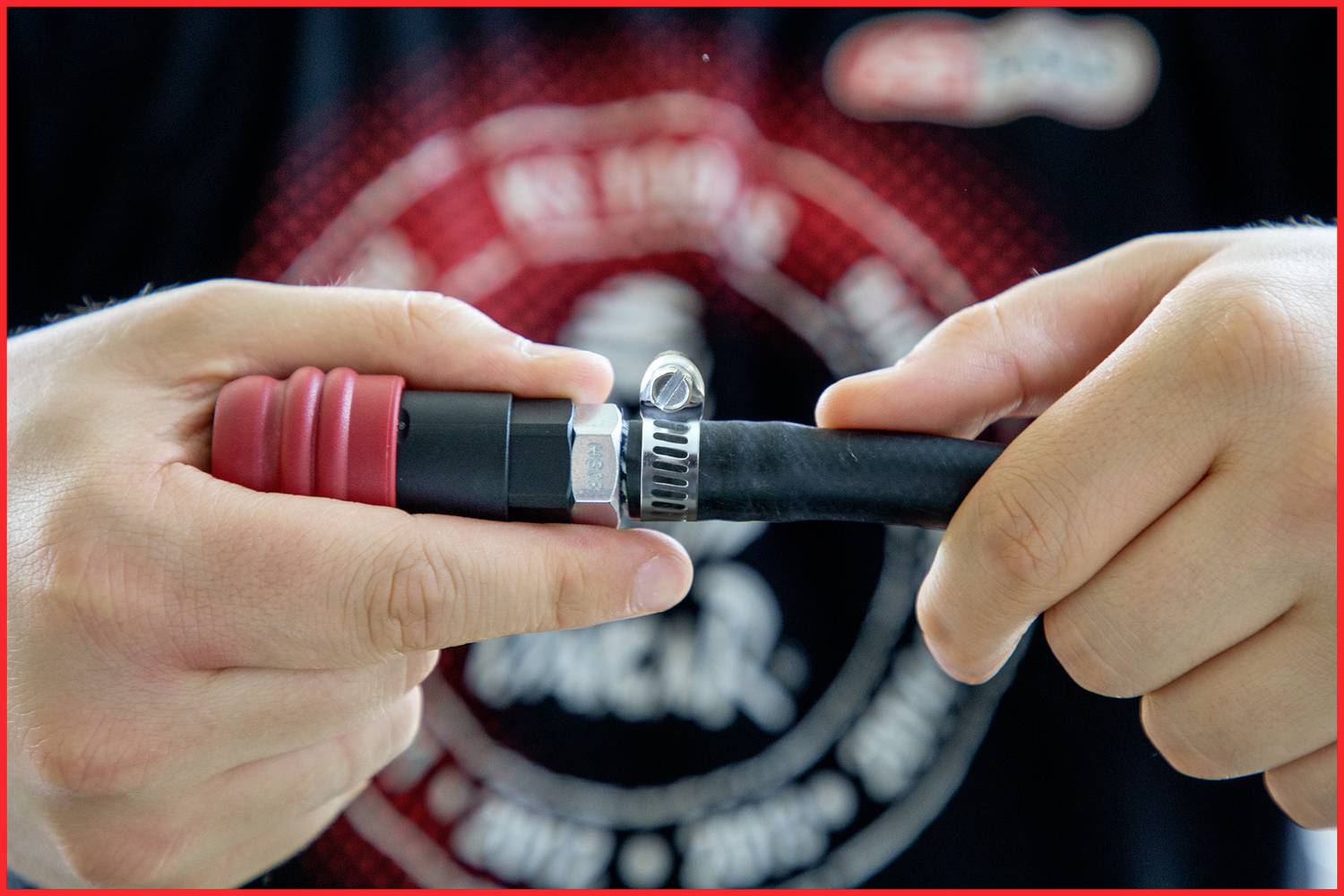 Two hands are securing a hose with a hose clip to a connection. Blurred clothing is visible in the background.