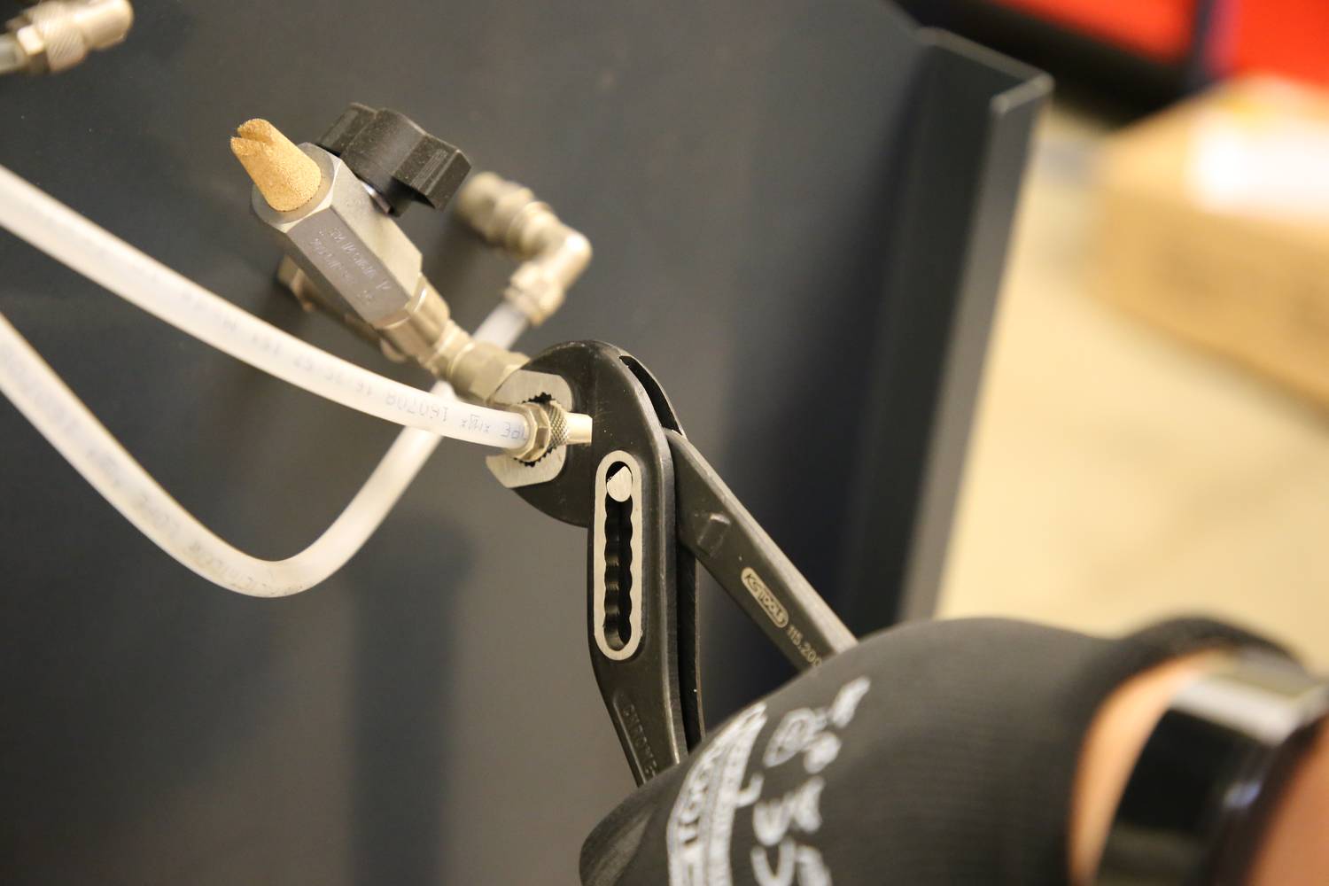 A person is tightening a screw on a pipe with a spanner while wearing protective gloves.