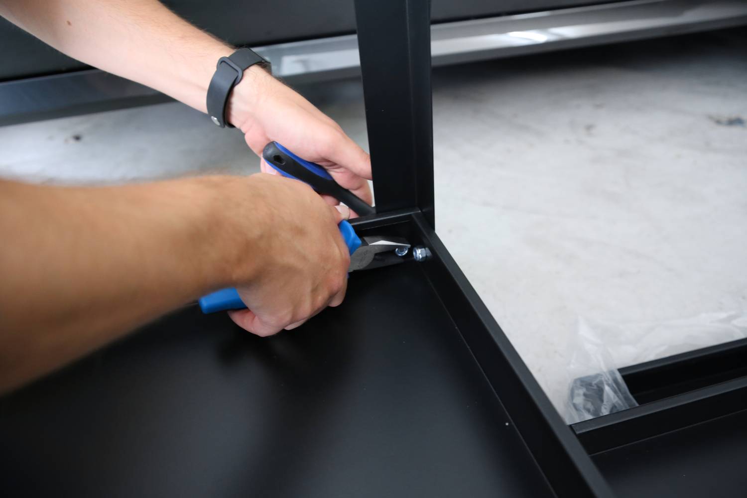 A person is assembling a black piece of furniture with a spanner.