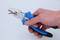 A hand is holding a blue pair of pliers and bending a thin wire with them.
