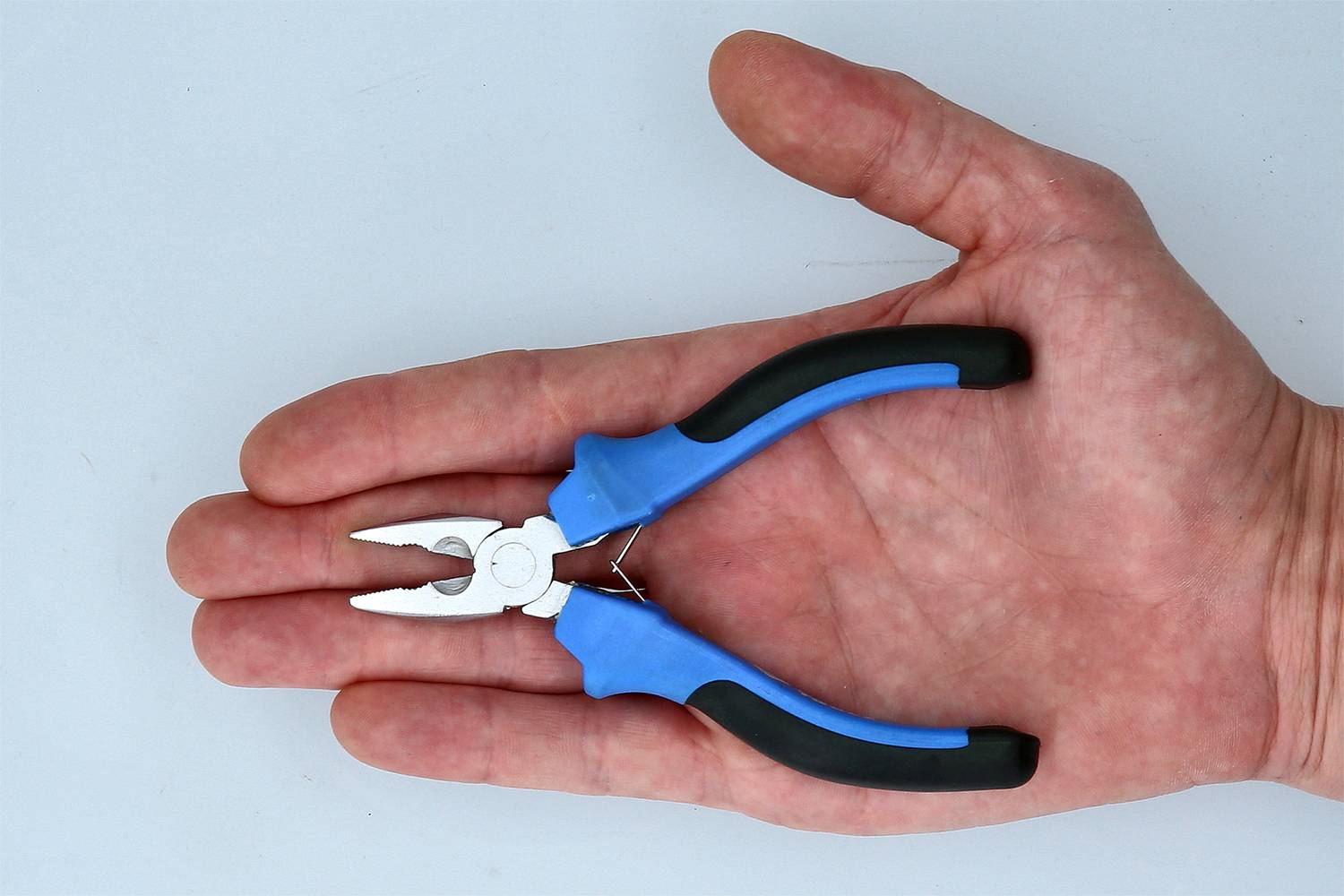 A hand is holding a small pair of pliers with blue-black handles, which are suitable for precision work.