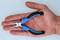 A hand is holding a small pair of pliers with blue handles. The pliers are open, revealing fine tips and black inserts on the handles.