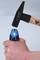 A hand holds a small hammer striking a blue screwdriver handle.