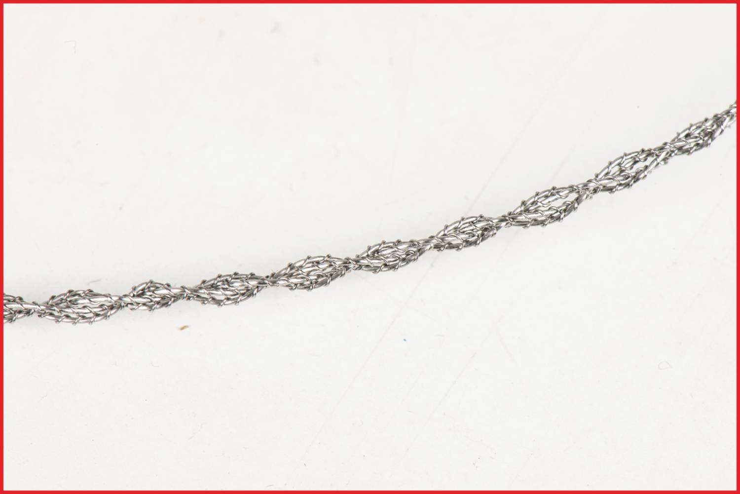Close-up of a twisted wire rope on a white background, framed by a red border. The wire is thin and intricately braided.