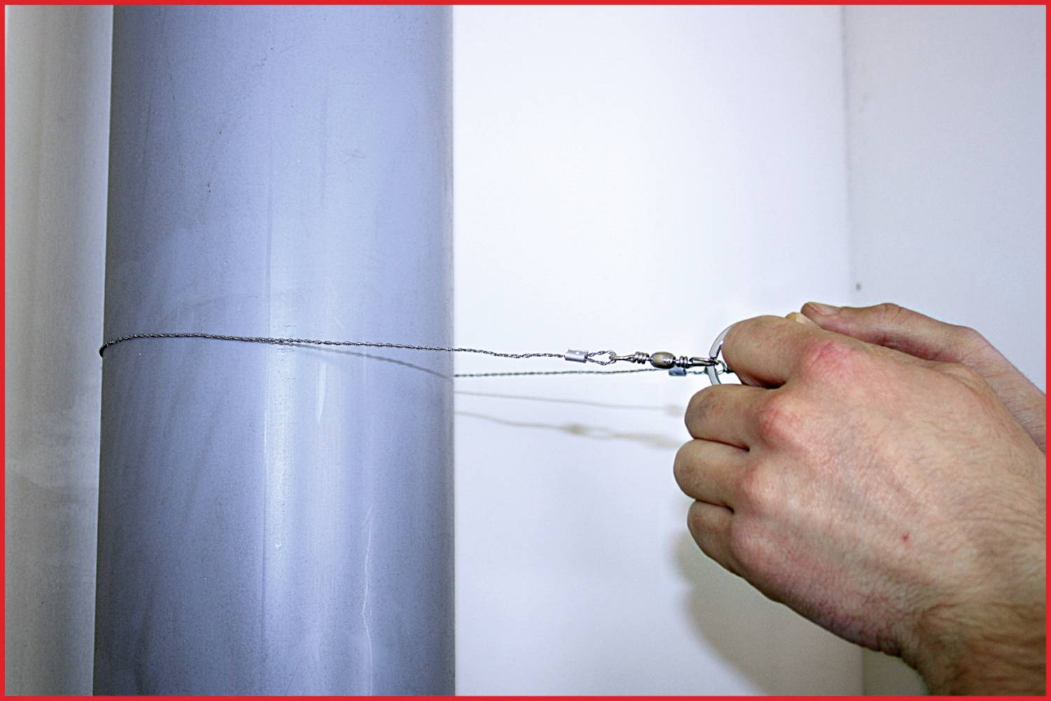 A hand stretches a wire around a thin pipe. The wire is secured with a tensioning device that generates pulling force.