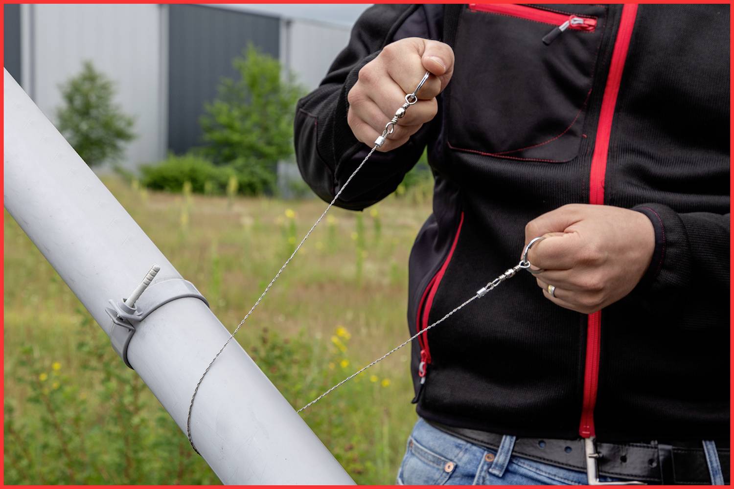 A person is stretching a wire cable on an angled metal pole in an industrial-looking area.