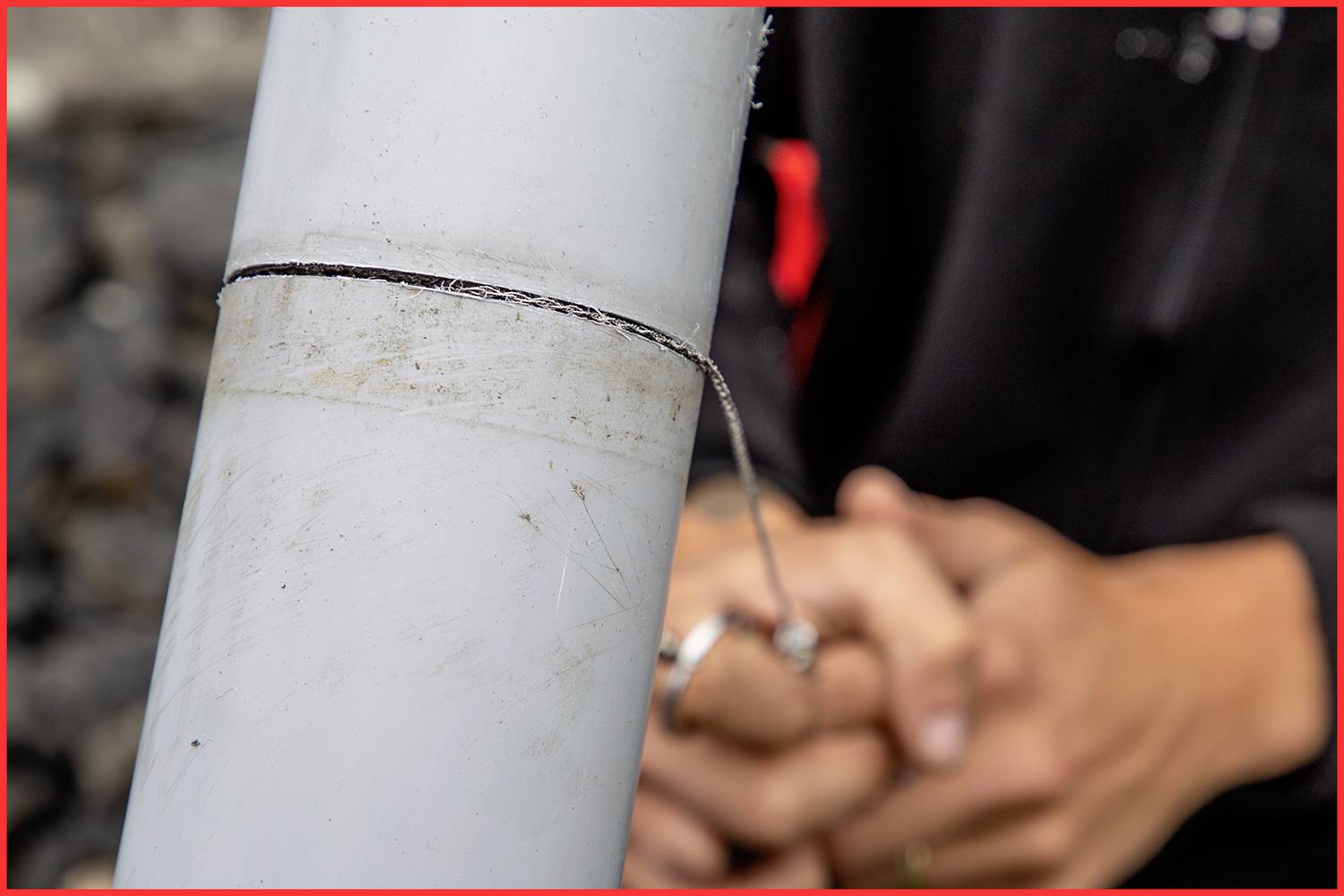 Close-up of a person working on a metal component. Hands are carefully folded in the background.