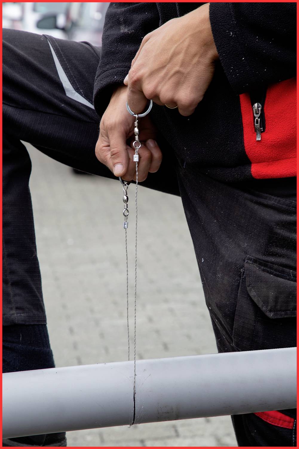 A person in a black and red outfit is turning a metal part in their hand. The background shows a paved surface.