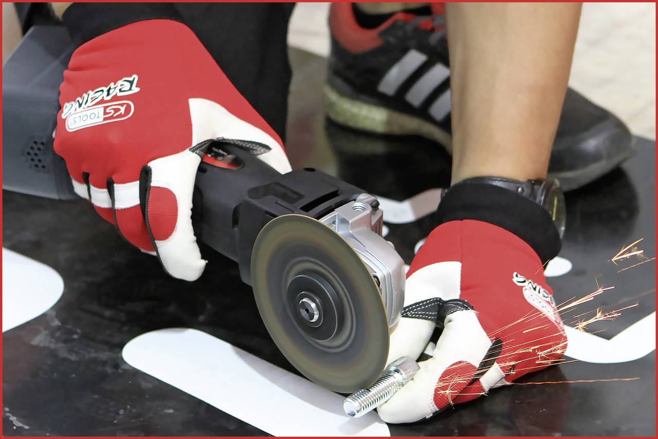 A person is wearing gloves and using a grinding machine to process a metal bolt. Sparks are flying from the point of contact.