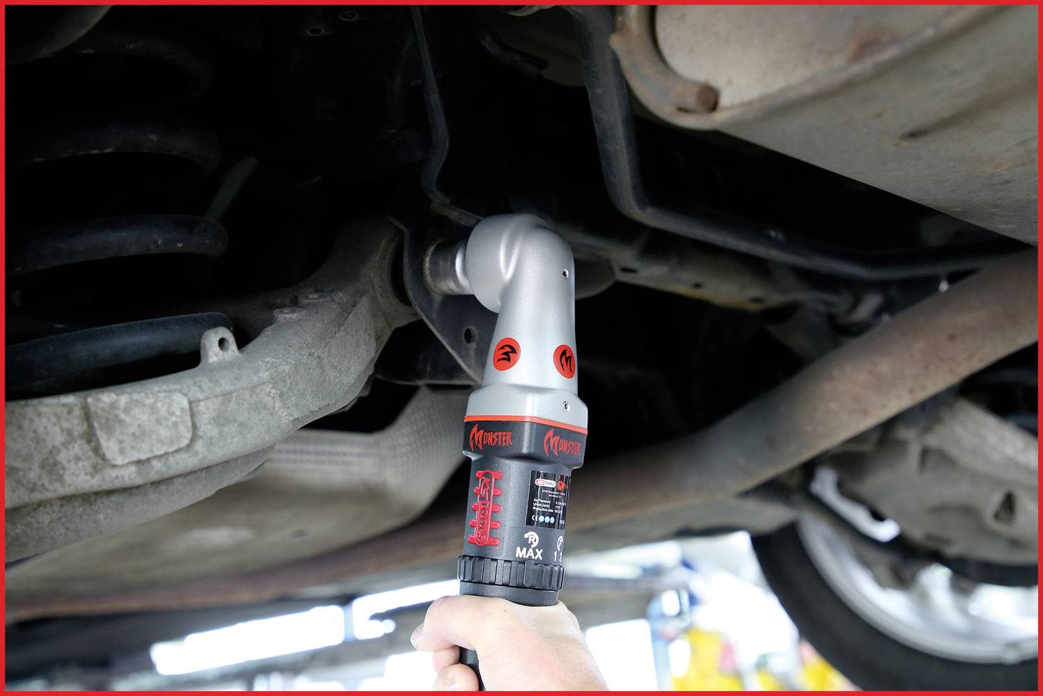 A person is using a hand tool to work underneath a vehicle's bodywork. The tool has a red and silver handle.