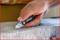 A hand cuts the plastic film from a cardboard box with a knife. The knife has a black handle and a metal blade.