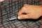 A hand is cutting a grey carpet with a carpet knife.