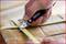 A hand cuts a stretched rubber band on a cardboard box using a folding knife.