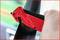 A hand is holding a red safety tool, about to cut through a black safety belt, with a blurred background.