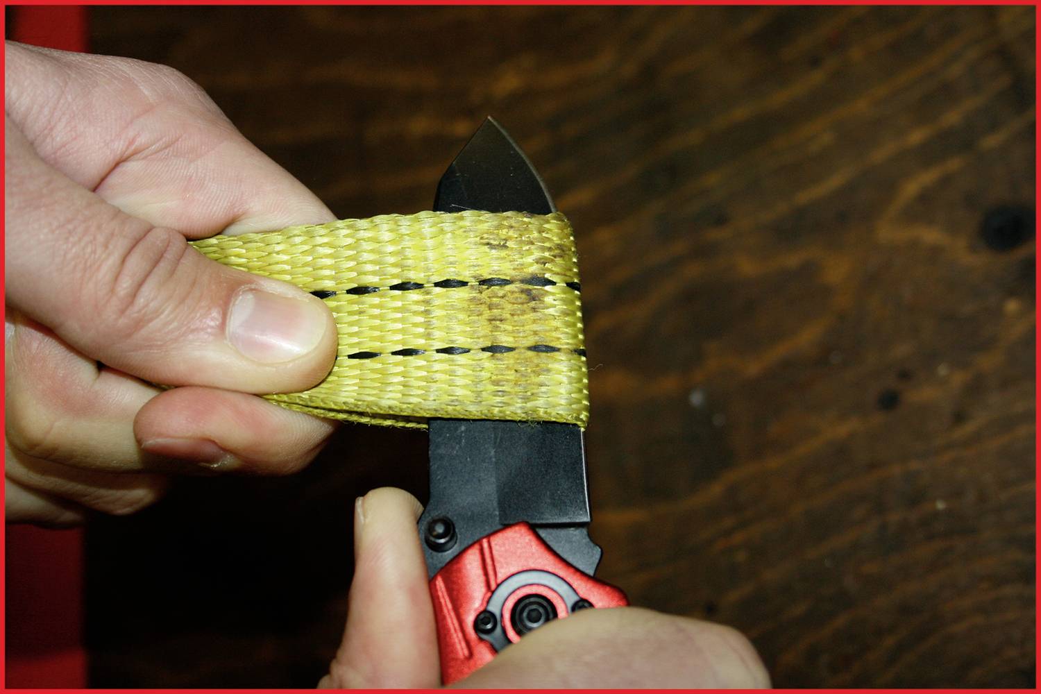 A person is cutting through a robust, yellow tape with a knife. The tape has black stripes and the background is made of wood.
