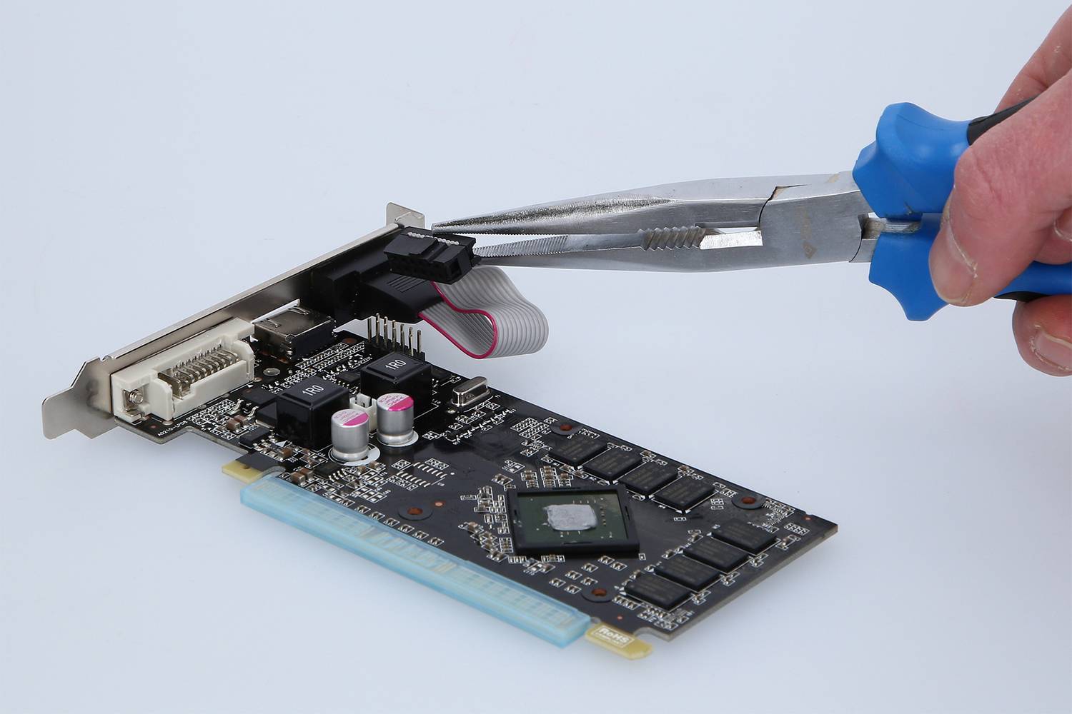 A hand holds pliers adjusting components on a circuit board. The board has multiple ports and electronic components.