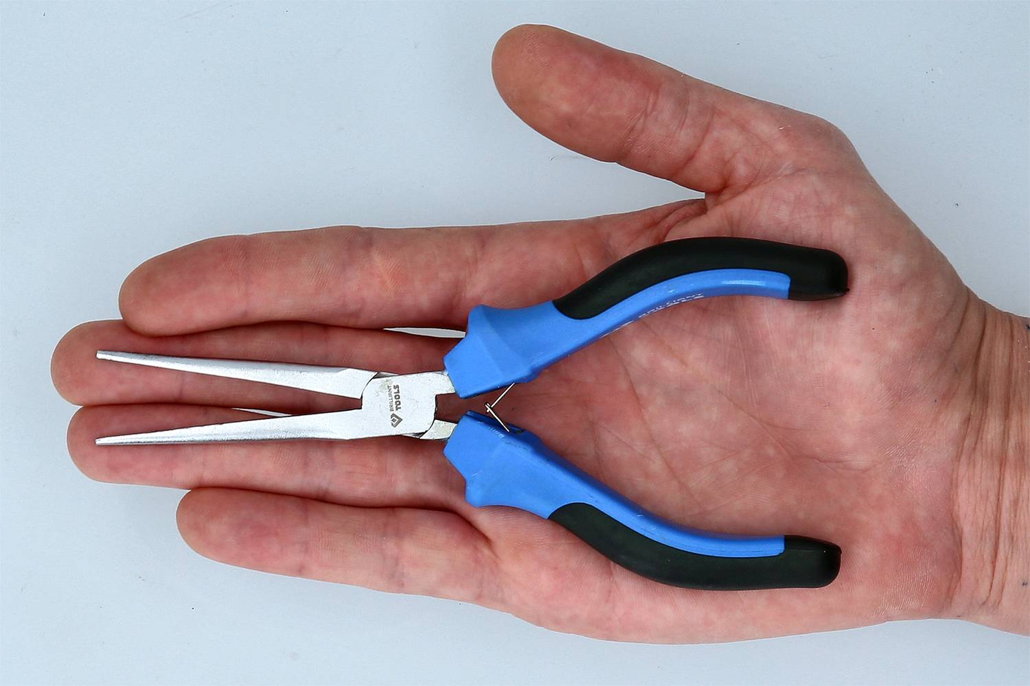 A hand is holding a small pair of pliers with blue handles and pointed, elongated jaws.