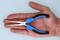 A hand is holding a small pair of pliers with blue handles and pointed, elongated jaws.